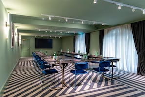 Una sala de conferencias con una larga mesa, sillas azules y una pantalla para proyector.