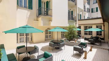 Un patio con mobiliario exterior, incluyendo mesas, sillas y sombrillas.