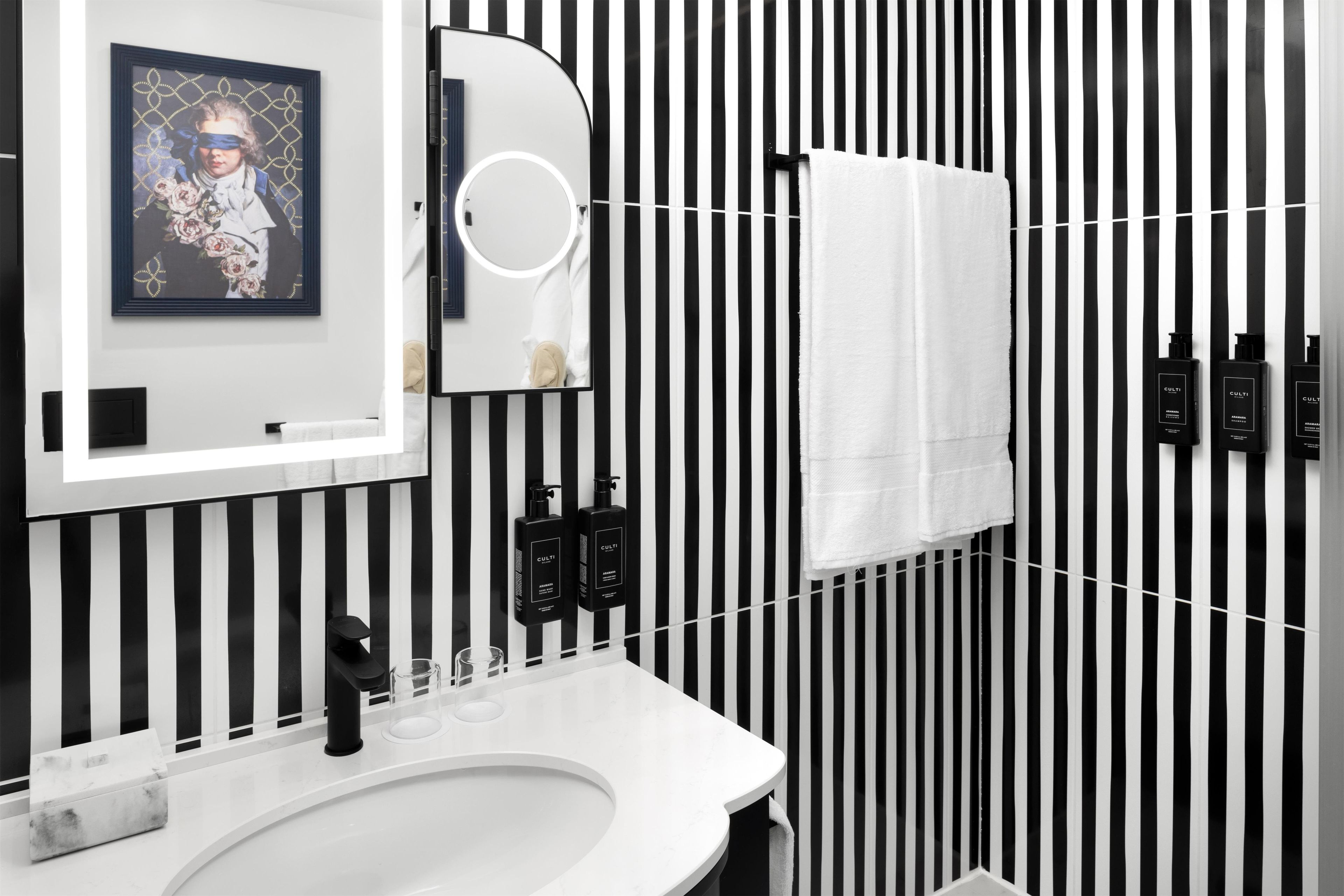 Un baño con un lavamanos blanco, un espejo, un perchero para toallas y rayas verticales negras en la pared.