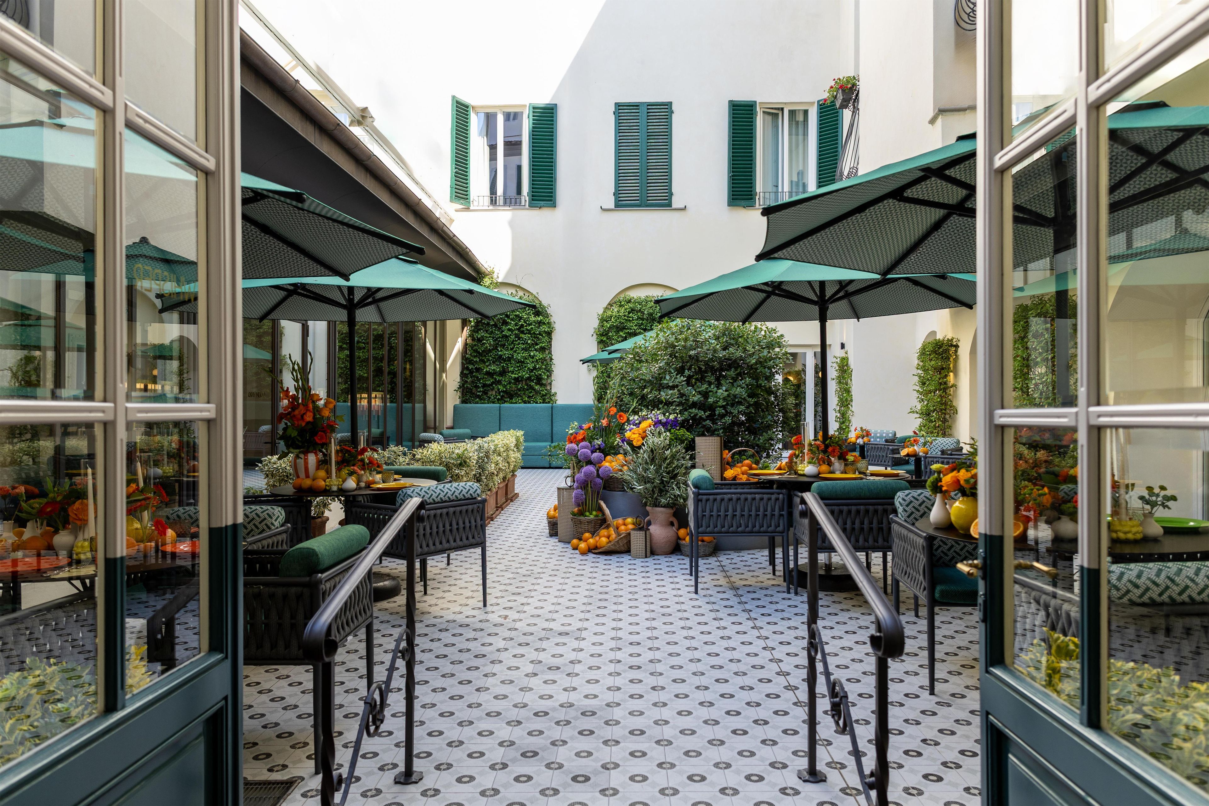 An outdoor seating area with tables and chairs, surrounded by greenery and potted plants.