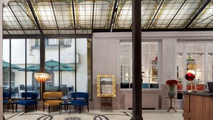 A lobby with a patterned floor, blue and yellow seating, a chandelier, and a mirror with a gold frame. - Anglo American Hotel Florence, Curio Collection by Hilton (Florence)