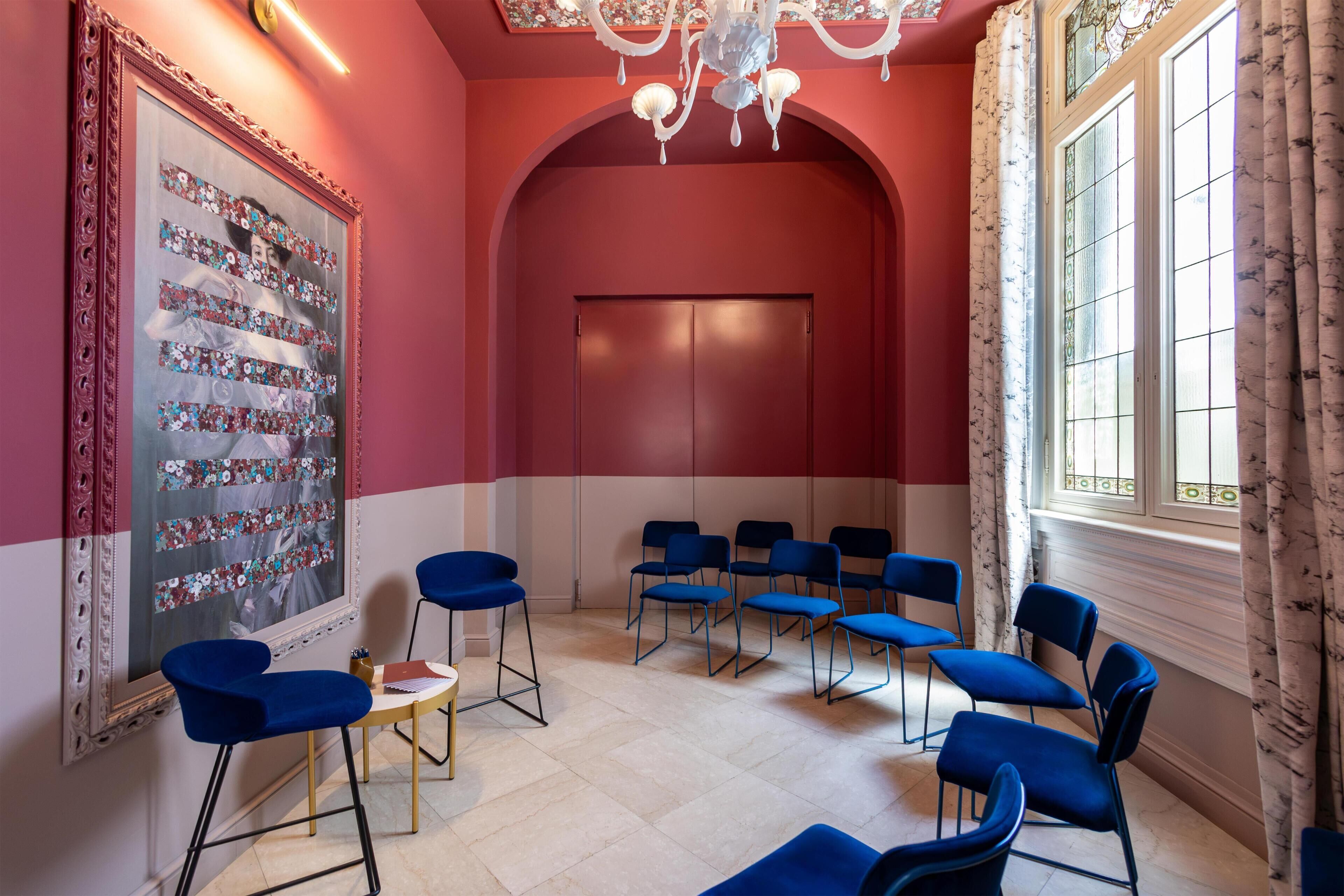A room with a red and white color scheme, a large mirror with floral decorations, and multiple blue chairs arranged for seating.