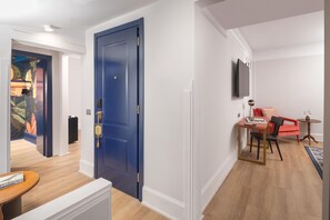 A modern hotel room with a blue door, a flat-screen TV mounted on the wall, a small table with a chair, and a red sofa. - Anglo American Hotel Florence, Curio Collection by Hilton (Florence)
