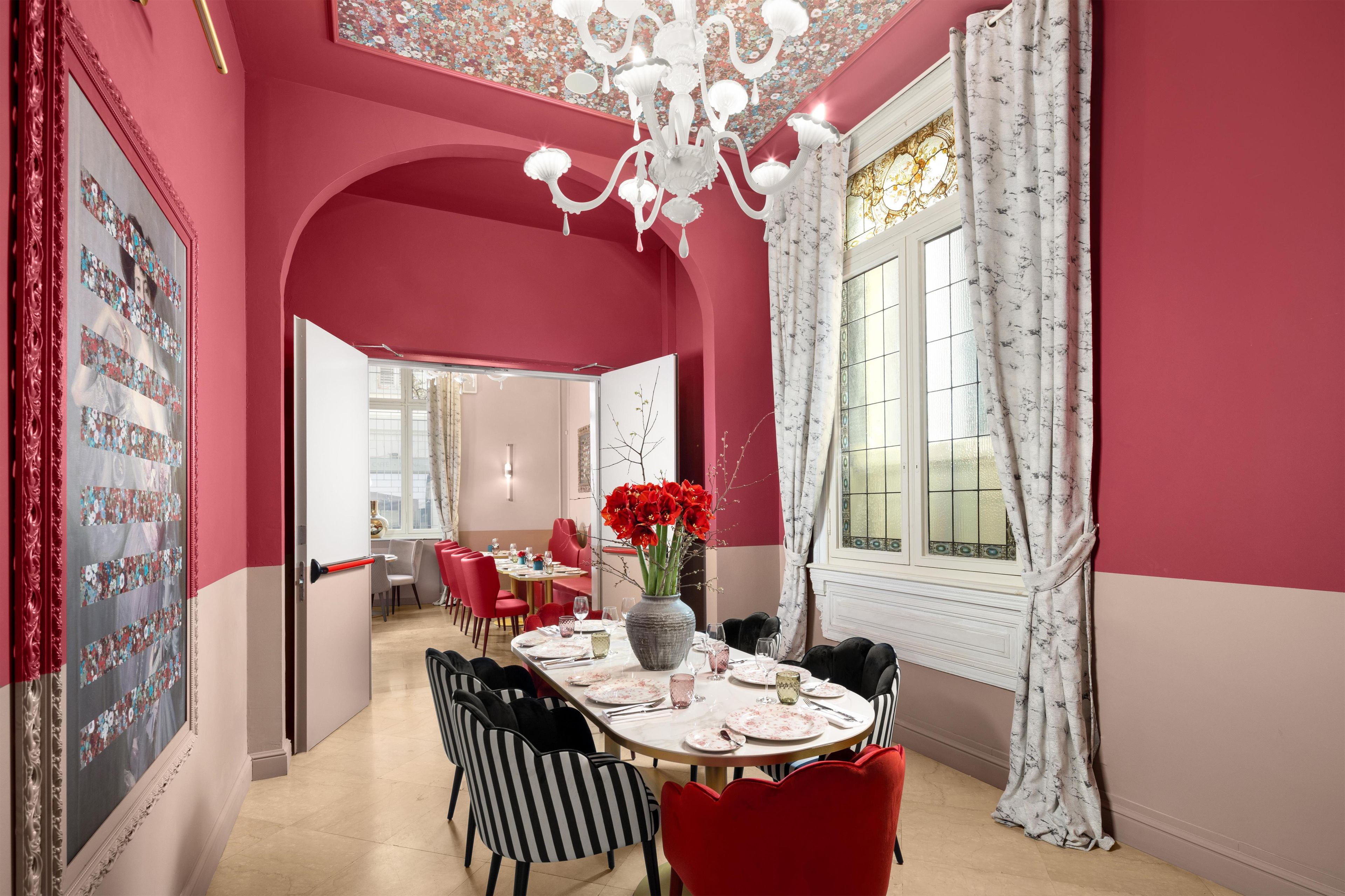 A dining room with a chandelier, red chairs, a table set for four, and a window with curtains.