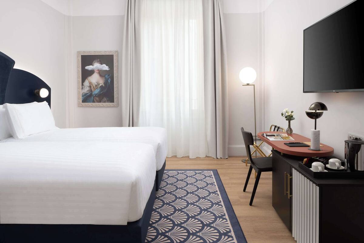 Ein Hotelzimmer mit einem Bett, einem Schreibtisch mit Stuhl, einem Flachbildfernseher und einem Bild an der Wand.