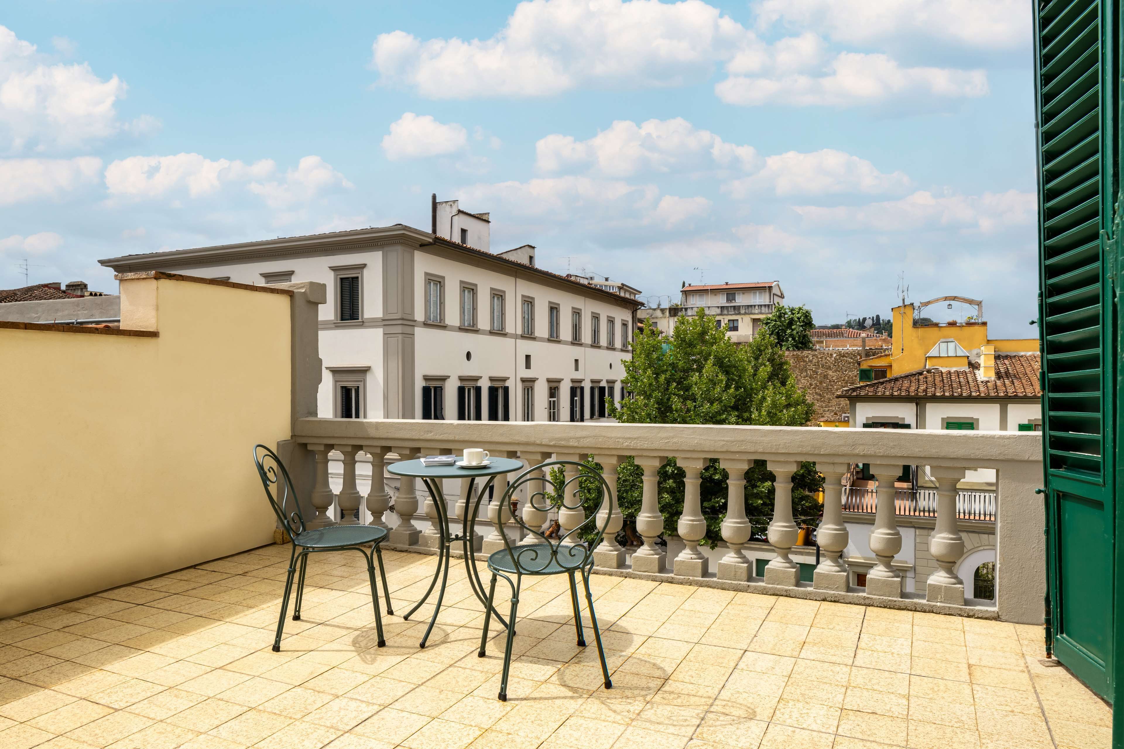 Un balcone con due sedie e un tavolo, affacciato su una città con edifici storici.