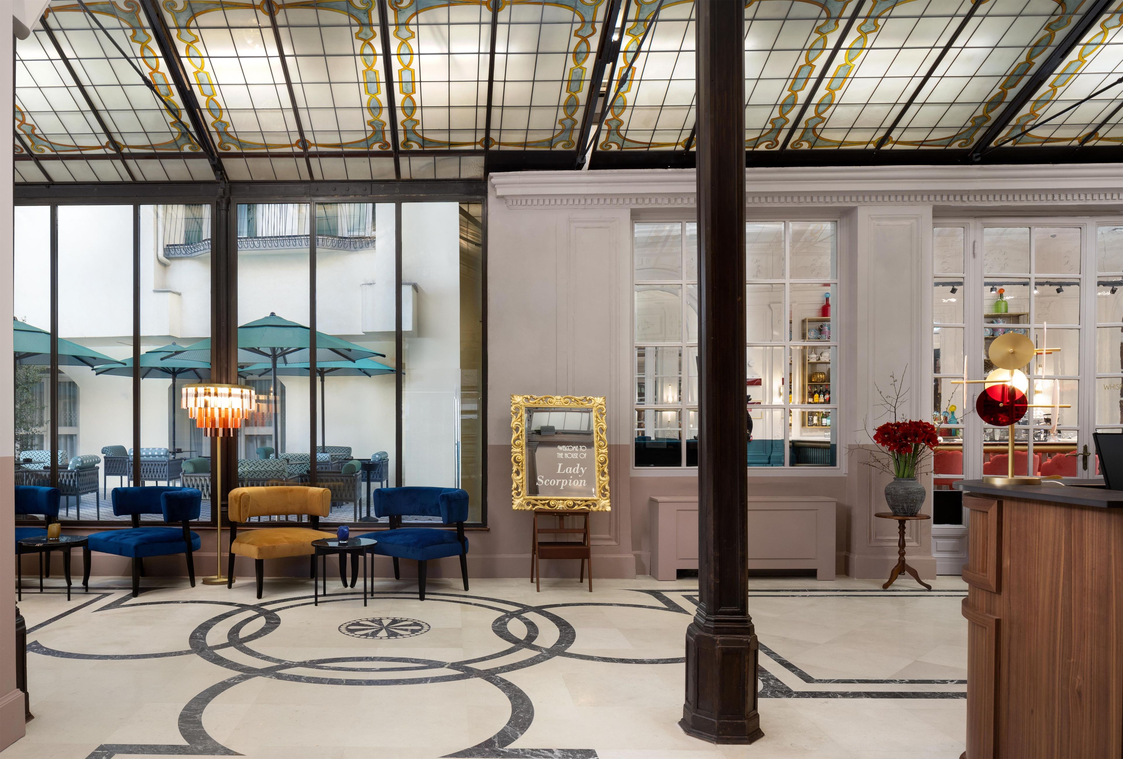 A hotel lobby with a large glass wall, a reception desk, and a seating area with blue chairs and a yellow sofa.