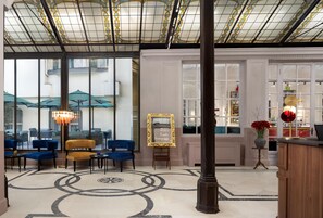 A hotel lobby with a large glass wall, a reception desk, and a seating area with blue chairs and a yellow sofa. - Anglo American Hotel Florence, Curio Collection by Hilton (Florence)