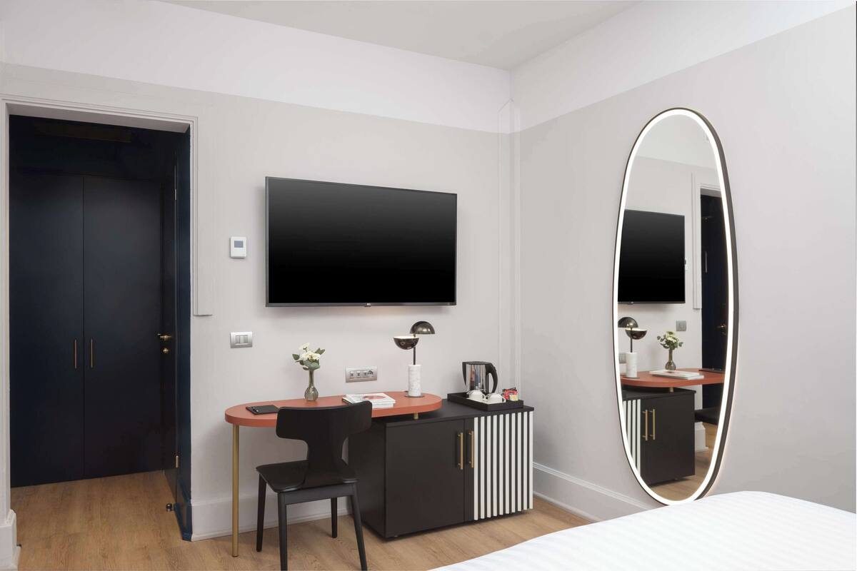 Ein modernes Hotelzimmer mit Flachbildfernseher, Schreibtisch mit Stuhl, großem Spiegel und Kleiderschrank.