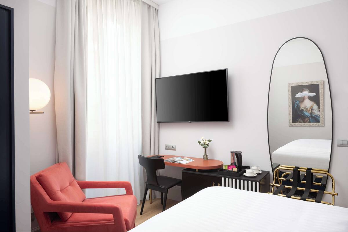 Ein Hotelzimmer mit Bett, Schreibtisch, Stuhl, Fernseher und einem großen Spiegel.