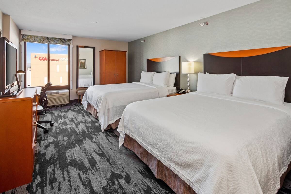 A hotel room with two beds, a desk, a chair, and a large window.