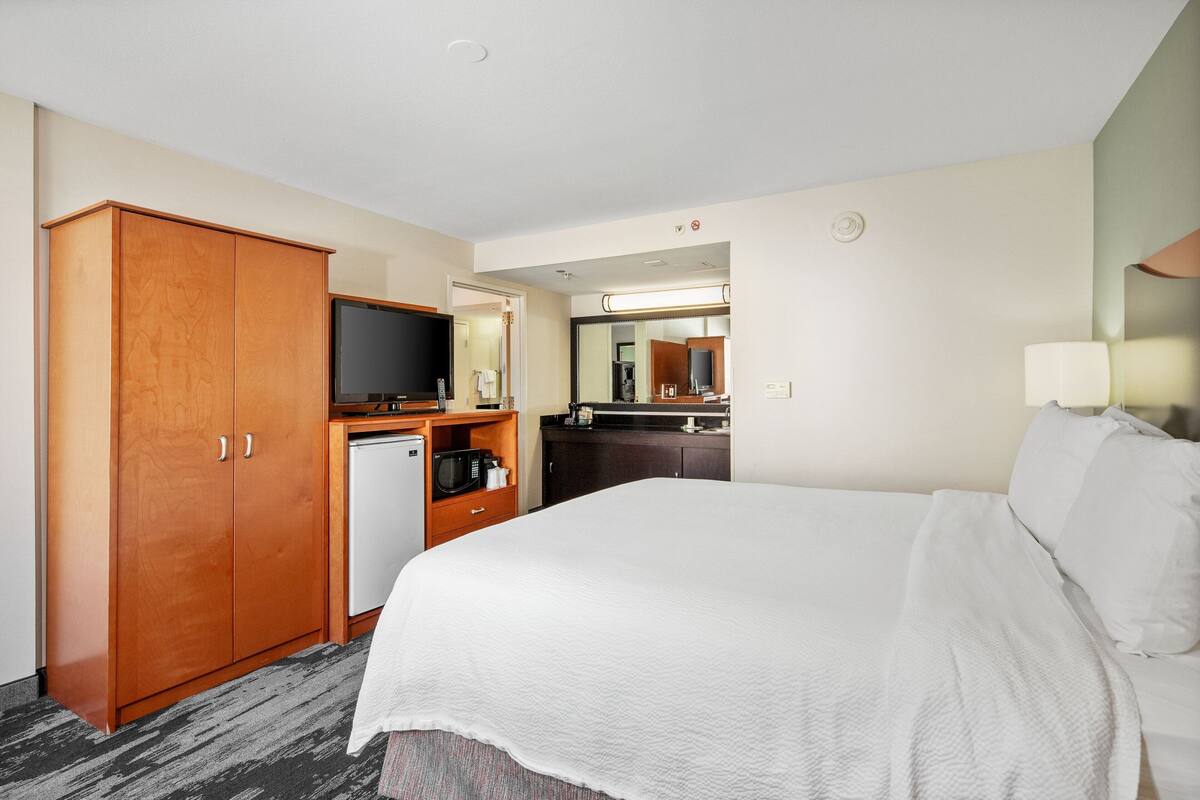 A hotel room with a large bed, a wardrobe, a small kitchenette, a television, and a mirror.