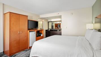 Quarto de hotel com cama grande, guarda-roupa, pequeno espaço de cozinha, televisão e espelho.