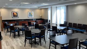 A spacious dining area with multiple tables and chairs, a wooden floor, and ceiling lights.