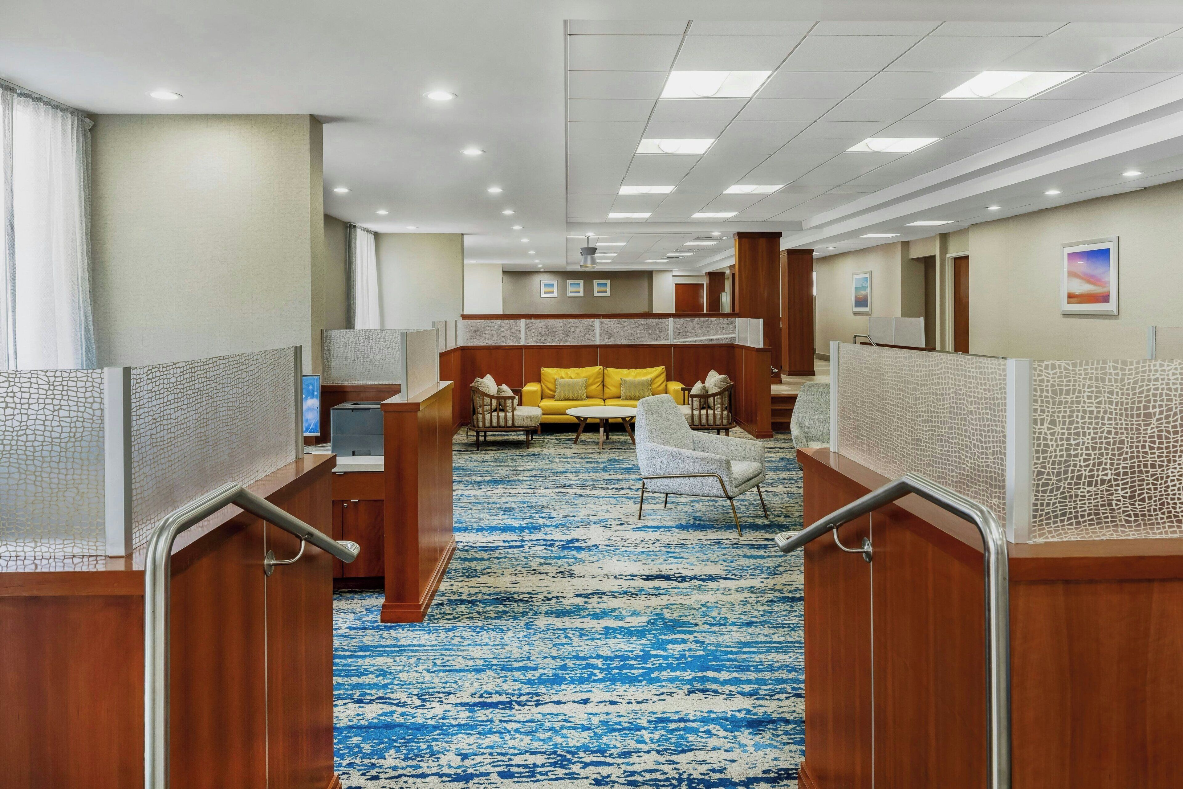 A hotel lobby with a blue patterned carpet, wooden furniture, and a yellow sofa.