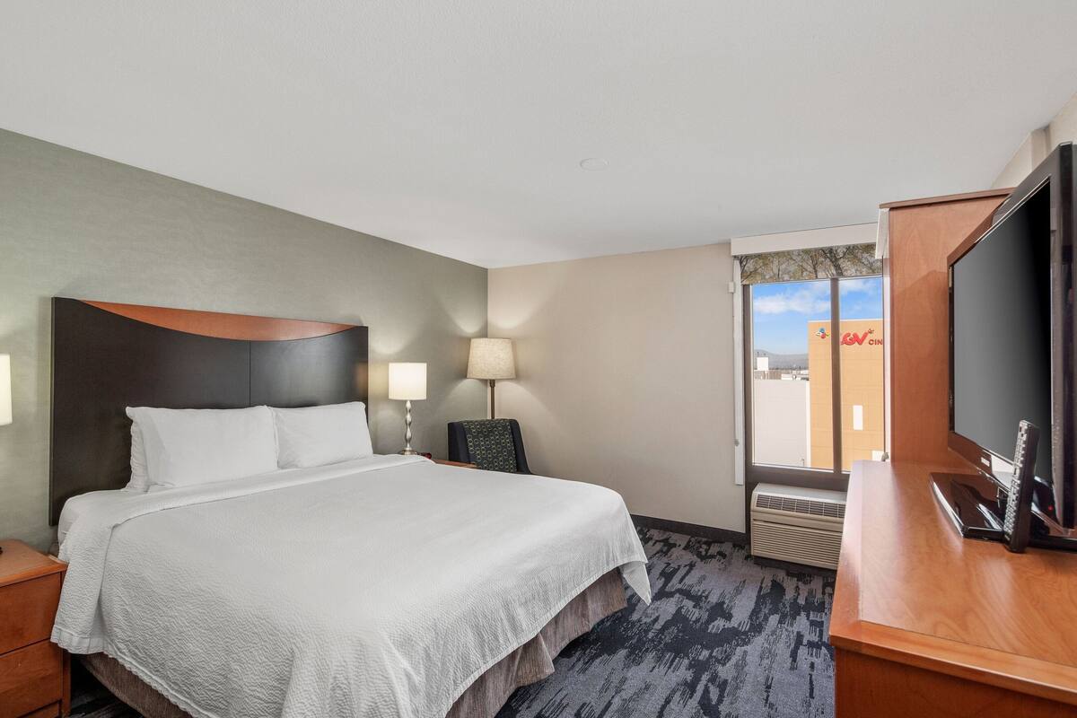 A hotel room with a bed, a desk with a TV, a chair, and a lamp.