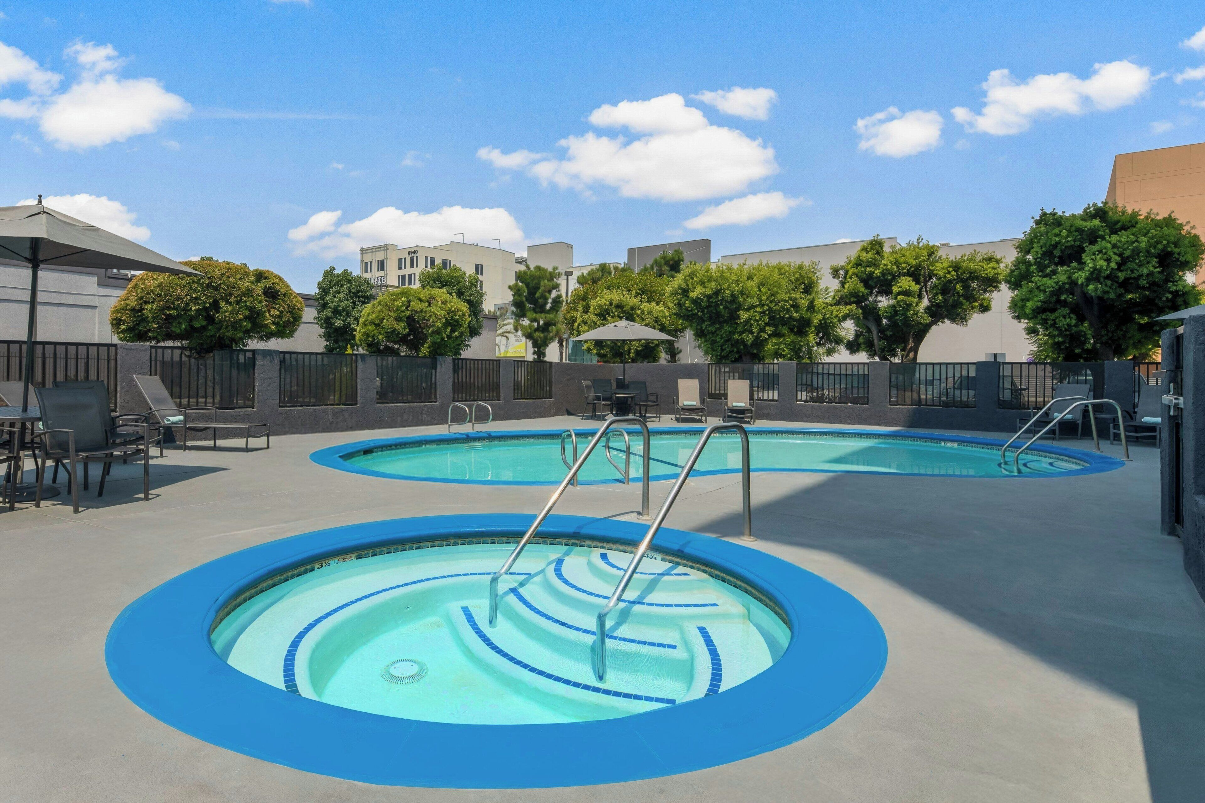 Un área de piscina en la azotea con dos piscinas circulares, sillas de descanso y vistas de edificios circundantes.