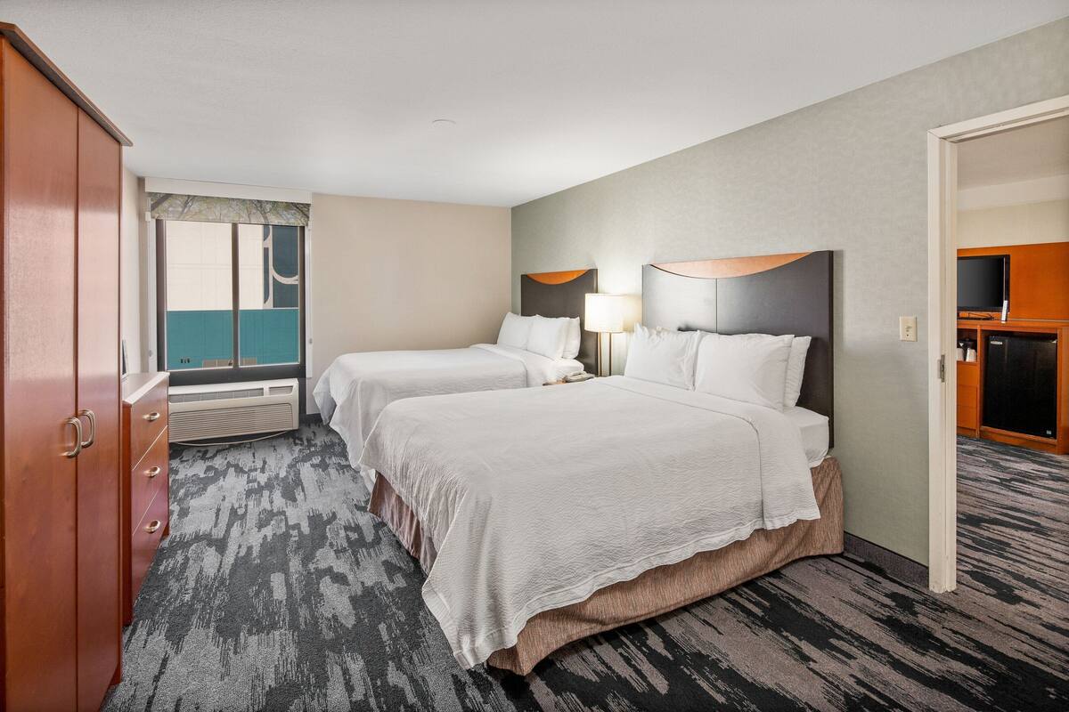 A hotel room with two beds, a wardrobe, a television, and a window with a view.