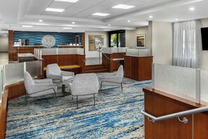 A modern hotel lobby with wooden paneling, a blue patterned carpet, and several seating areas. - Fairfield Inn & Suites Anaheim North/Buena Park. (Buena Park)