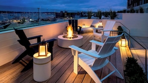 Une terrasse sur le toit avec un foyer, des fauteuils Adirondack blancs et des lanternes.