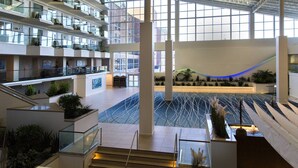 Un atrium à plusieurs niveaux, doté de rampes en verre, d’un élément décoratif central en eau et de plantes d’intérieur.