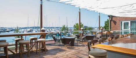 Una terraza de madera con asientos exteriores, un bar y vistas a barcos y agua.