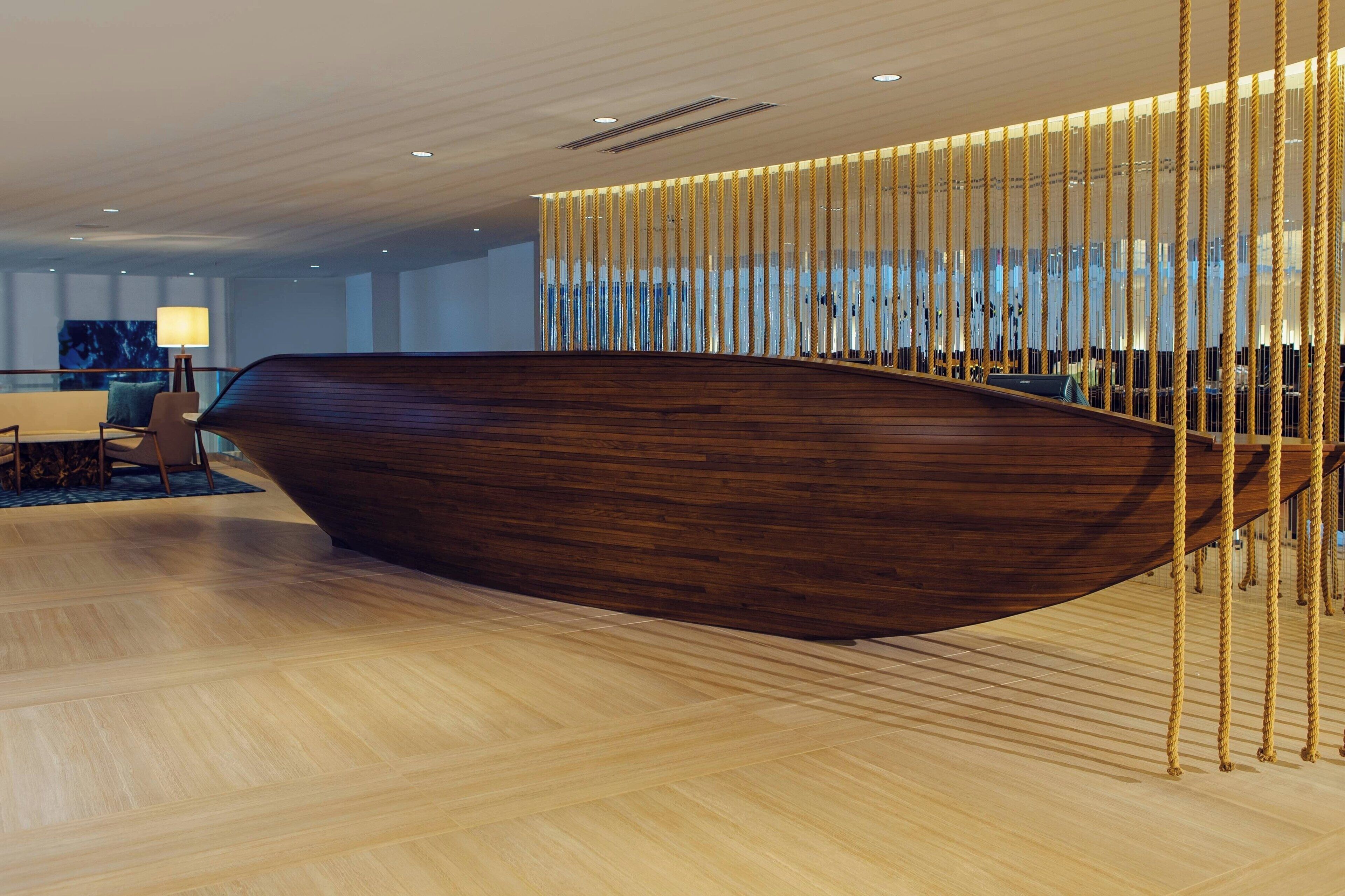A modern interior with a wooden boat-shaped seating area, a wooden floor, and a vertical rope barrier.