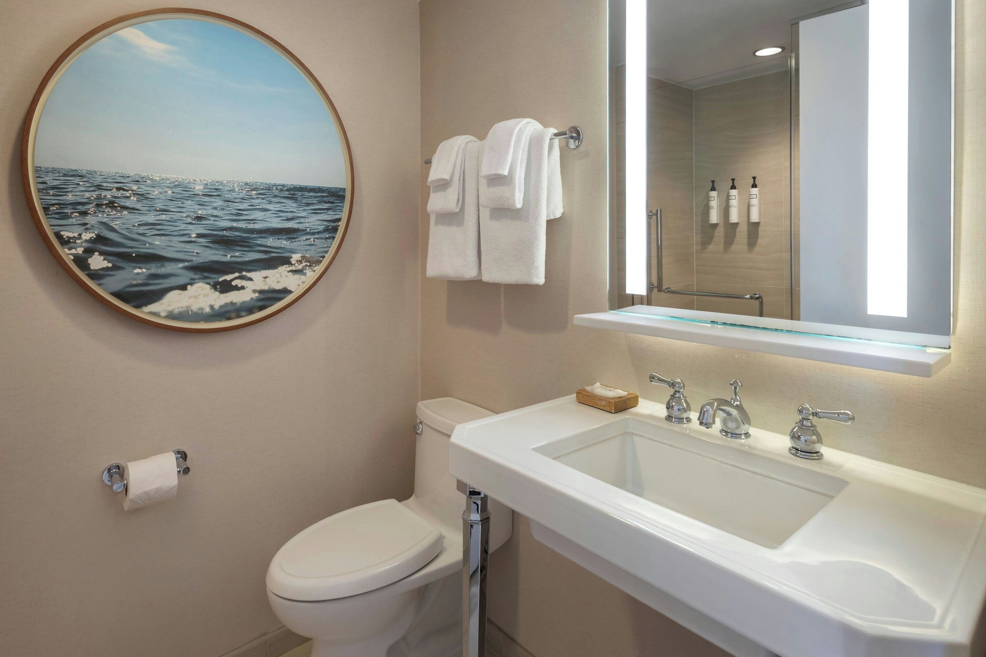 Un baño con inodoro, lavamanos y un espejo redondo.