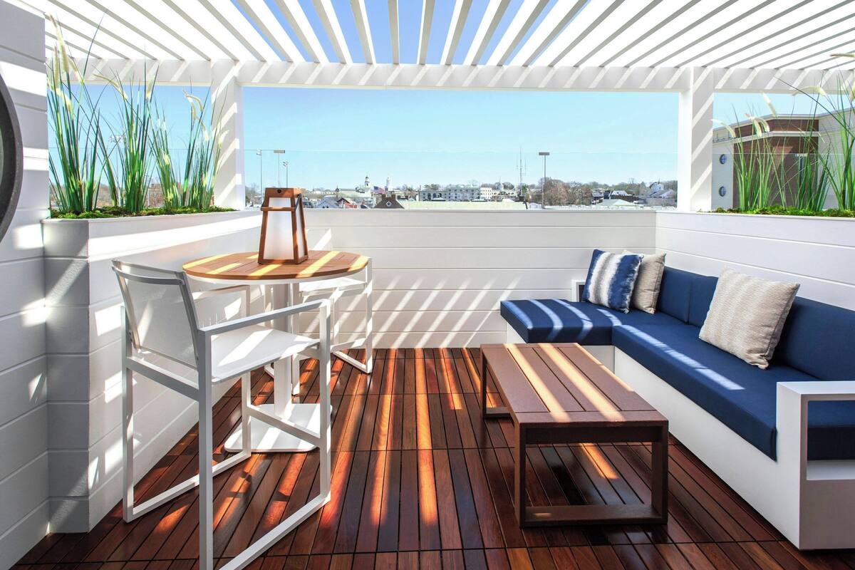 A modern outdoor seating area with a wooden floor, white furniture, and a view of a cityscape.