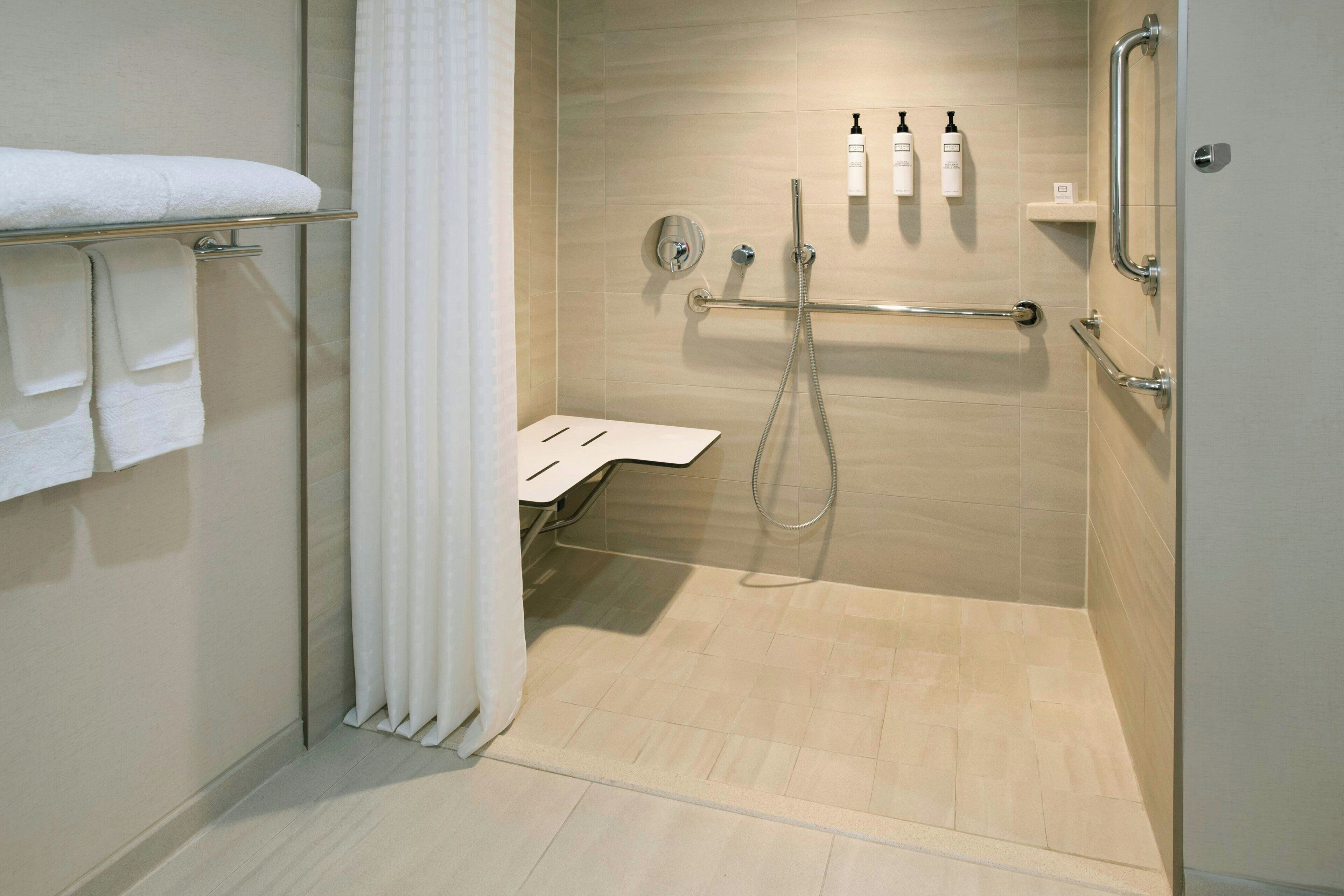 A modern bathroom with a walk-in shower, grab bars, a towel rack, and a toilet.