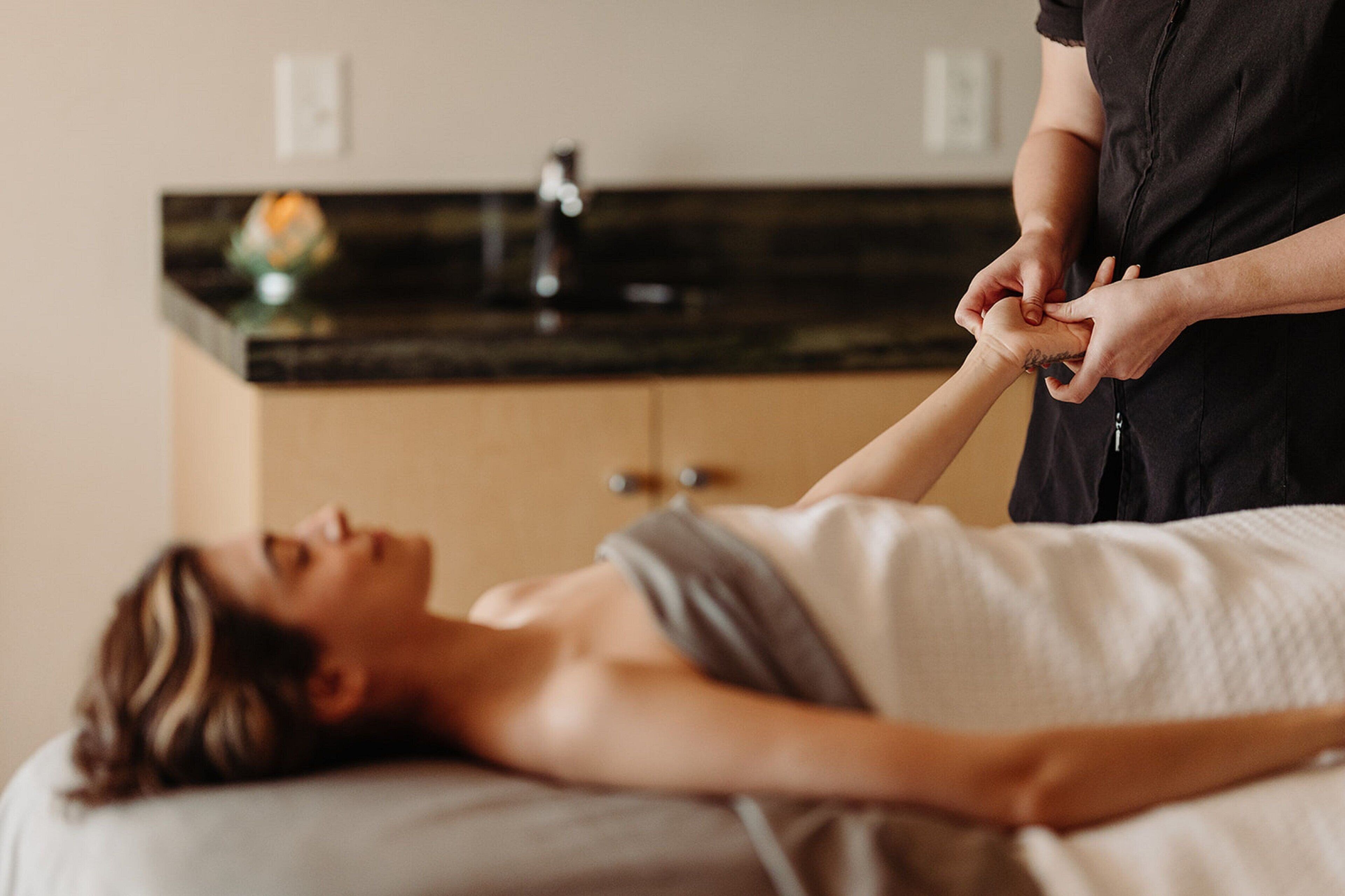 A person lying on a massage table receiving a hand massage.
