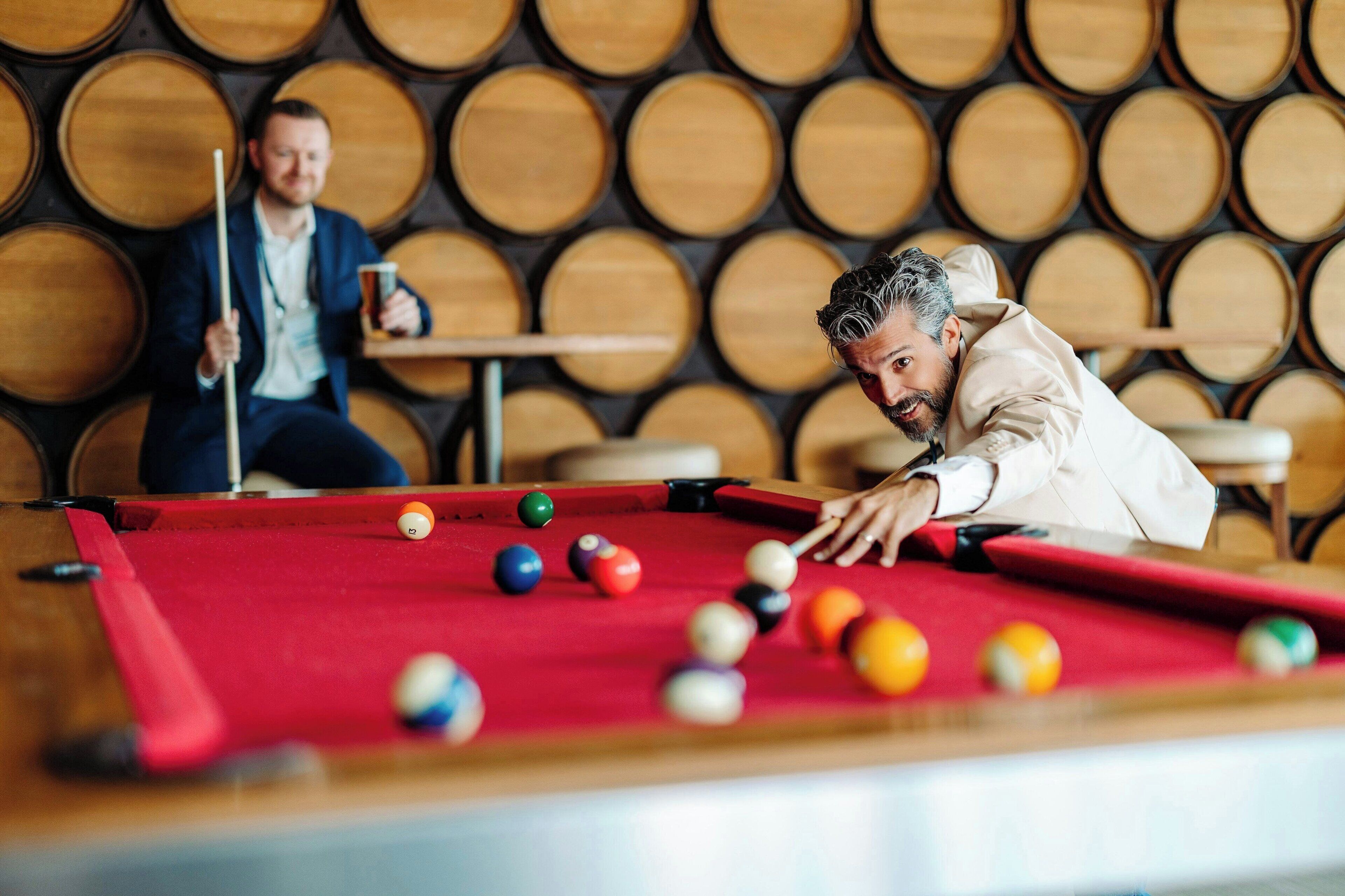 Une table de billard avec des billes et une personne qui joue, le tout sur fond de barils en bois.