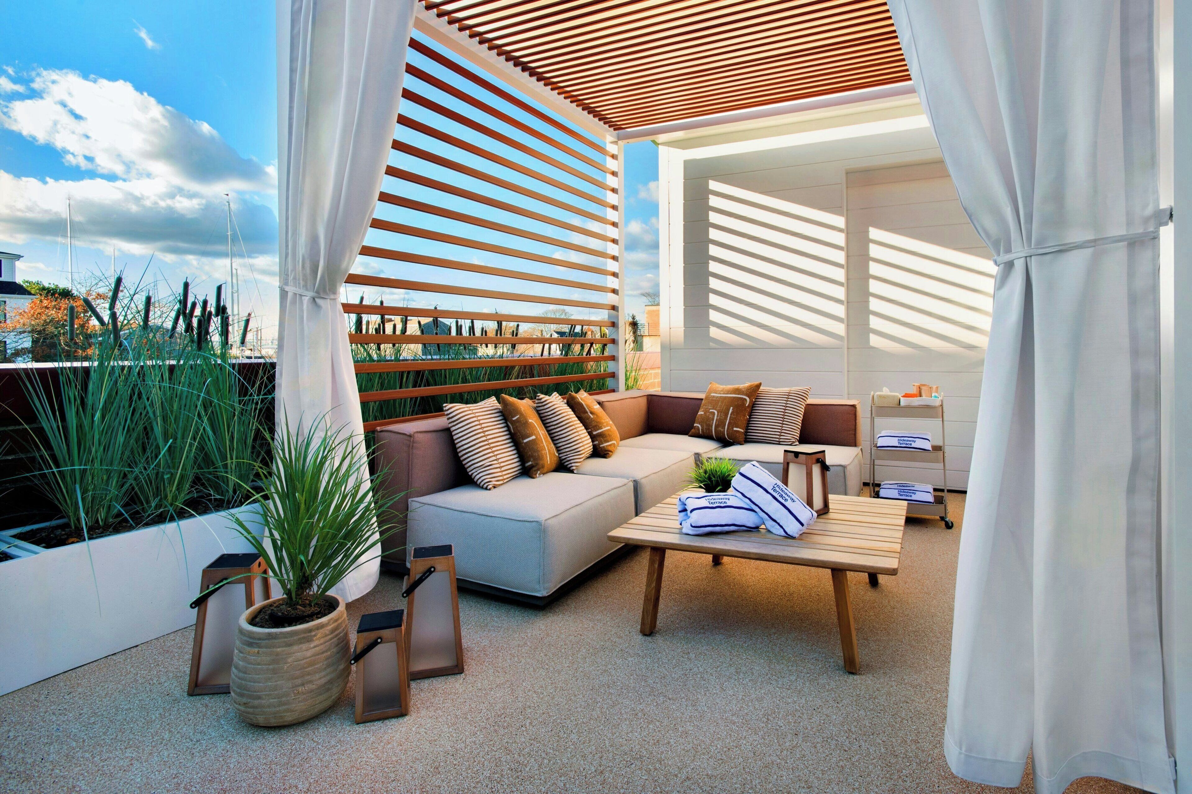 A modern outdoor living space with a sofa, cushions, a coffee table, and a potted plant.