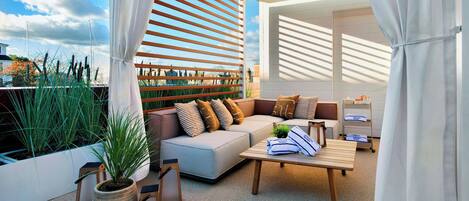 A modern outdoor living space with a sofa, cushions, a coffee table, and a potted plant.