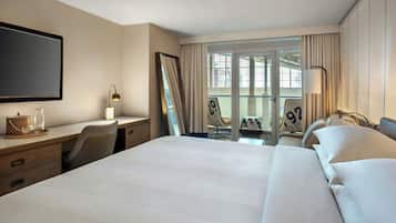 A hotel room with a large bed, a desk with a lamp, a chair, and a view of the outdoors through a large window.