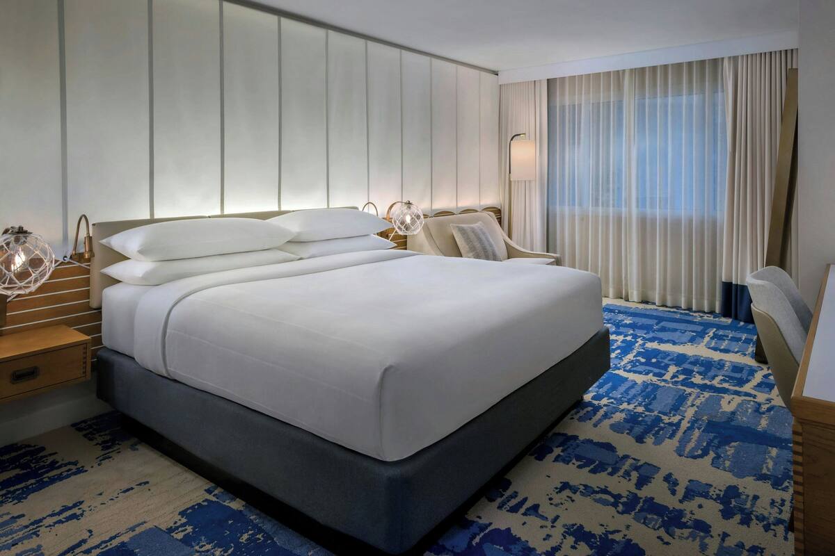 A modern hotel room with a large bed, a desk, and a chair.