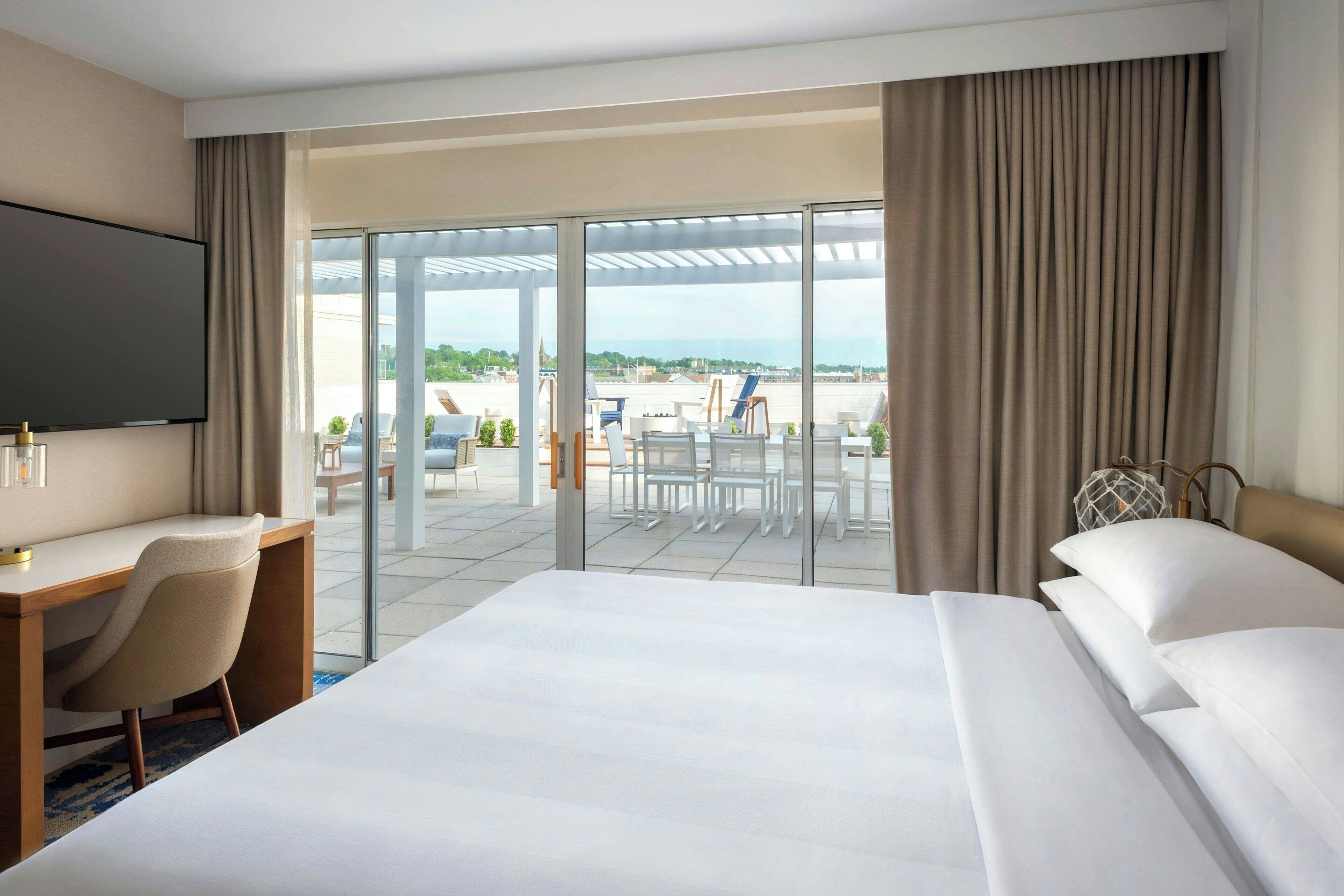 Une chambre d’hôtel avec un grand lit, un bureau et une chaise. Elle dispose d’un balcon avec vue sur la plage et la mer.