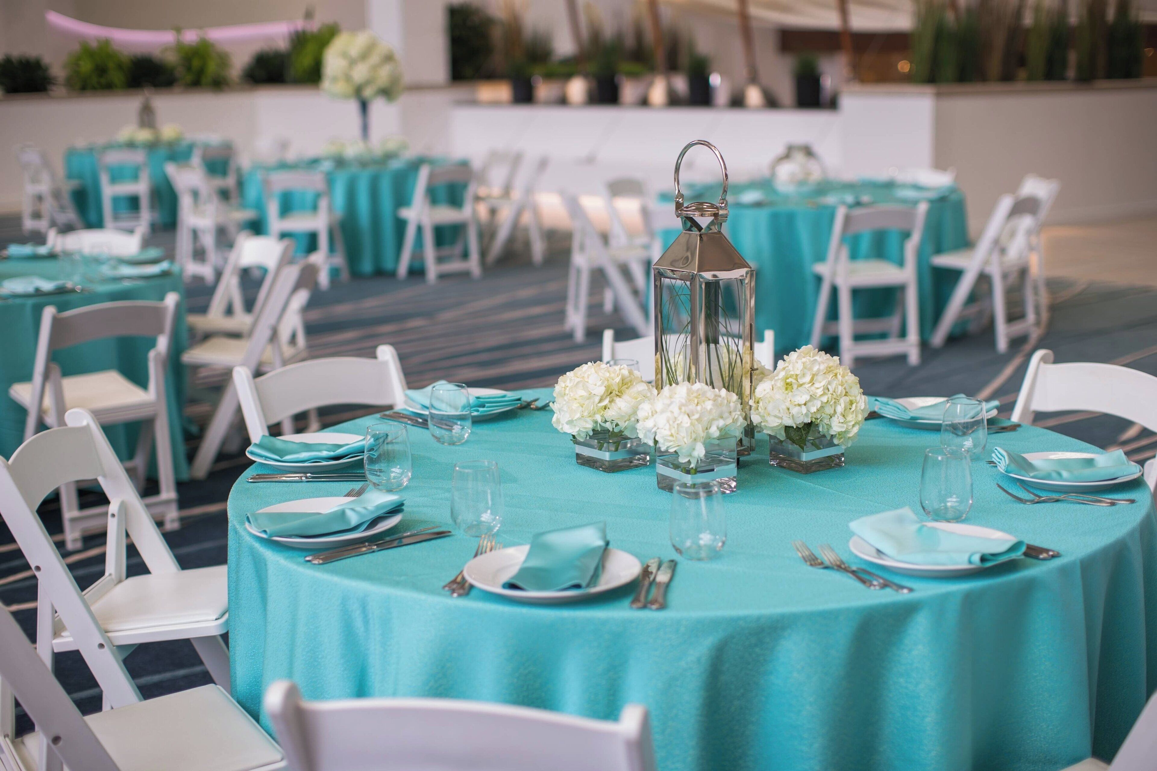 A banquet hall with round tables covered in teal tablecloths, white chairs, and floral centerpieces.