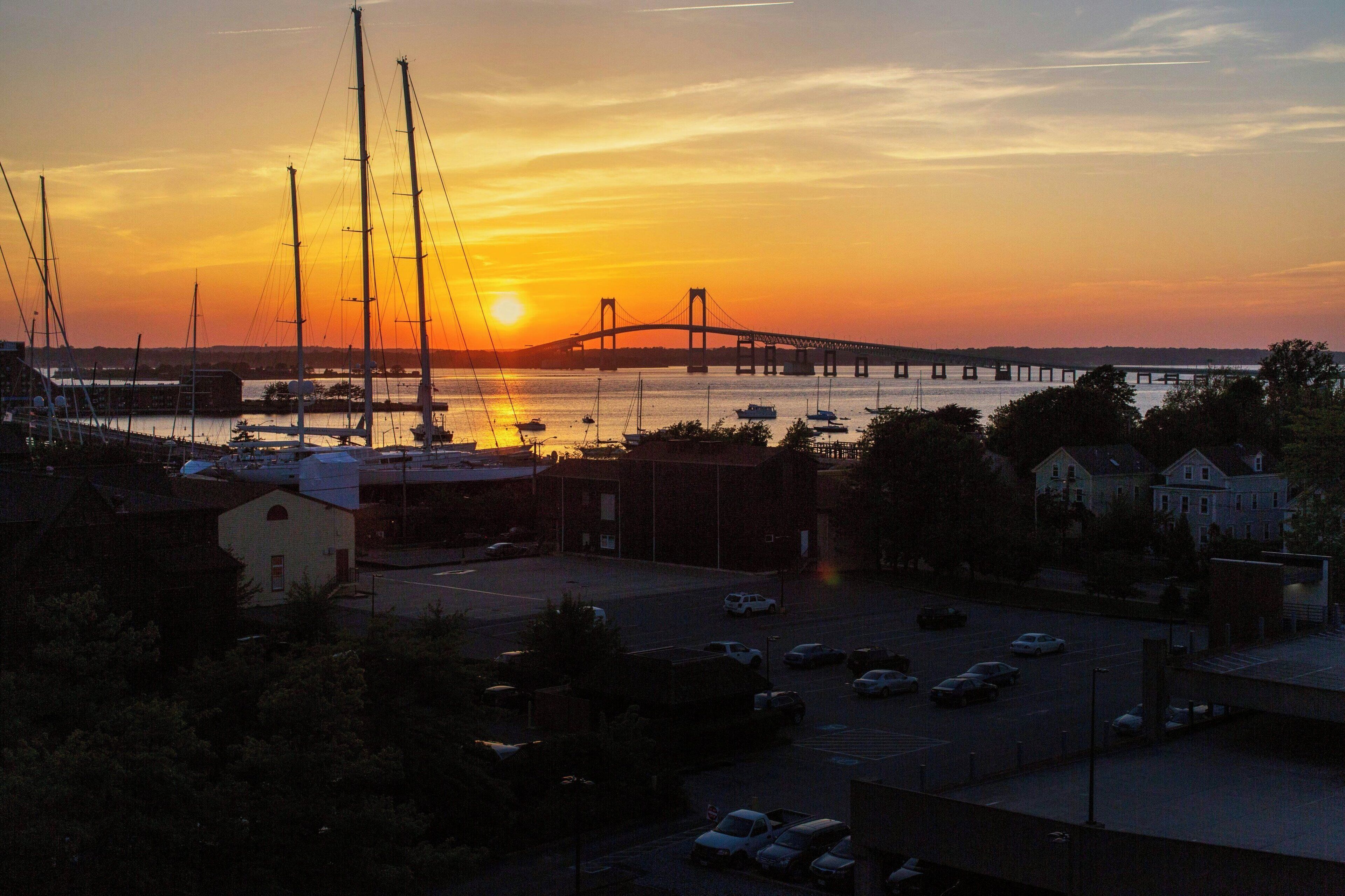 A sunset view over a bridge, boats, and a parking lot with buildings in the foreground.