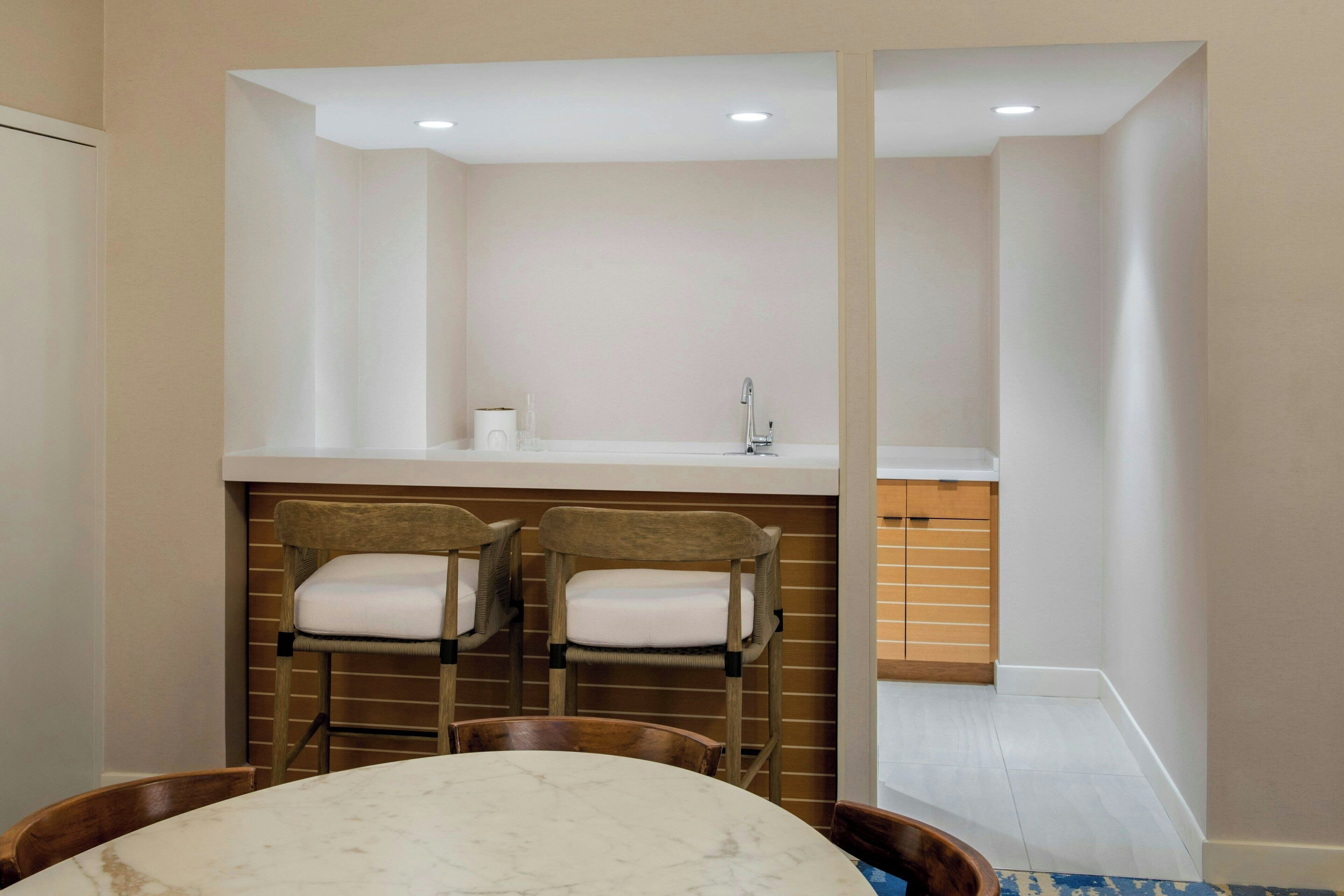 Un baño moderno con un lavabo blanco, dos sillas de madera y una mesa con encimera de mármol.