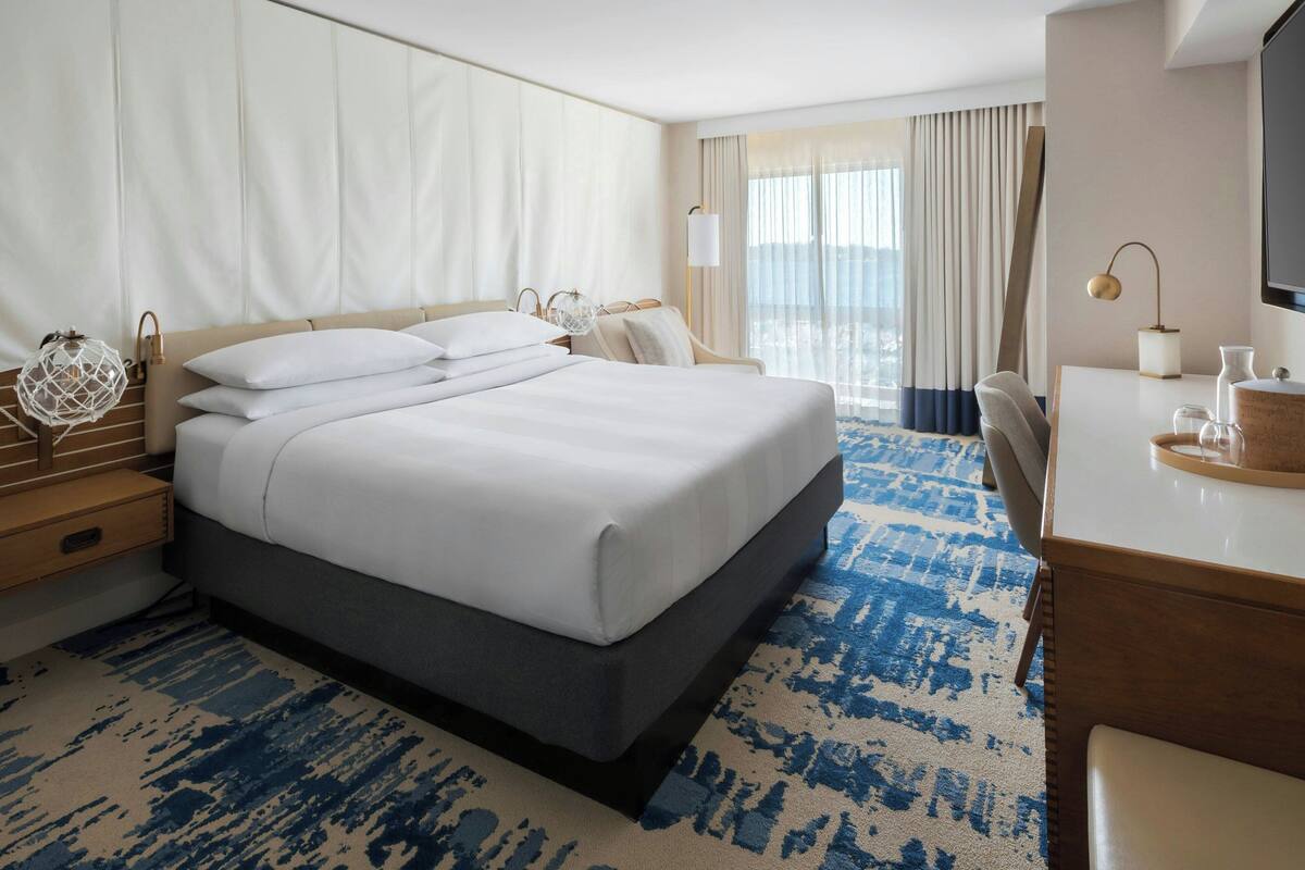 A hotel room with a large bed, a desk with a chair, a TV, and a window with curtains.