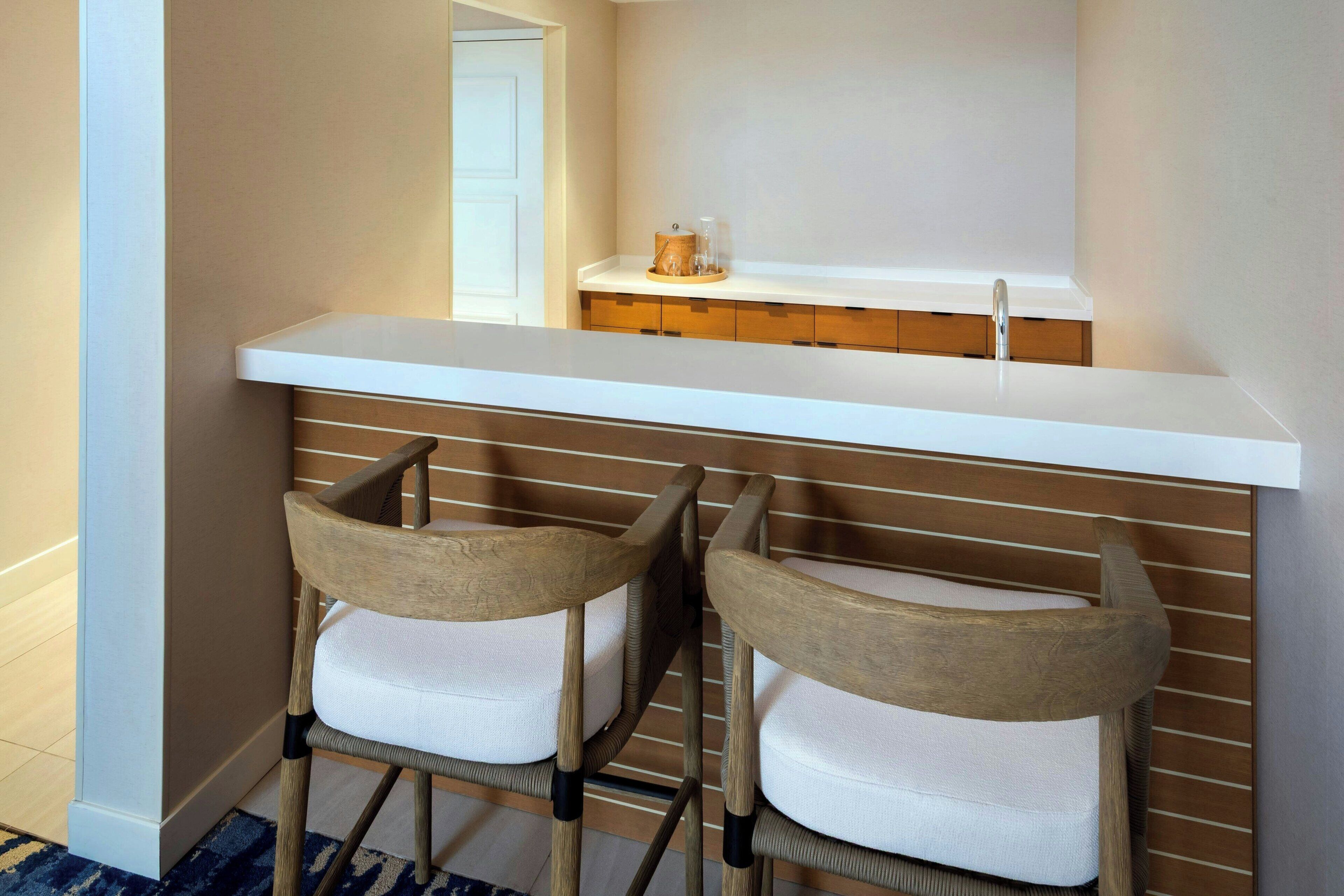 A kitchen with a white countertop, two wooden chairs with white cushions, and a wooden cabinet below.