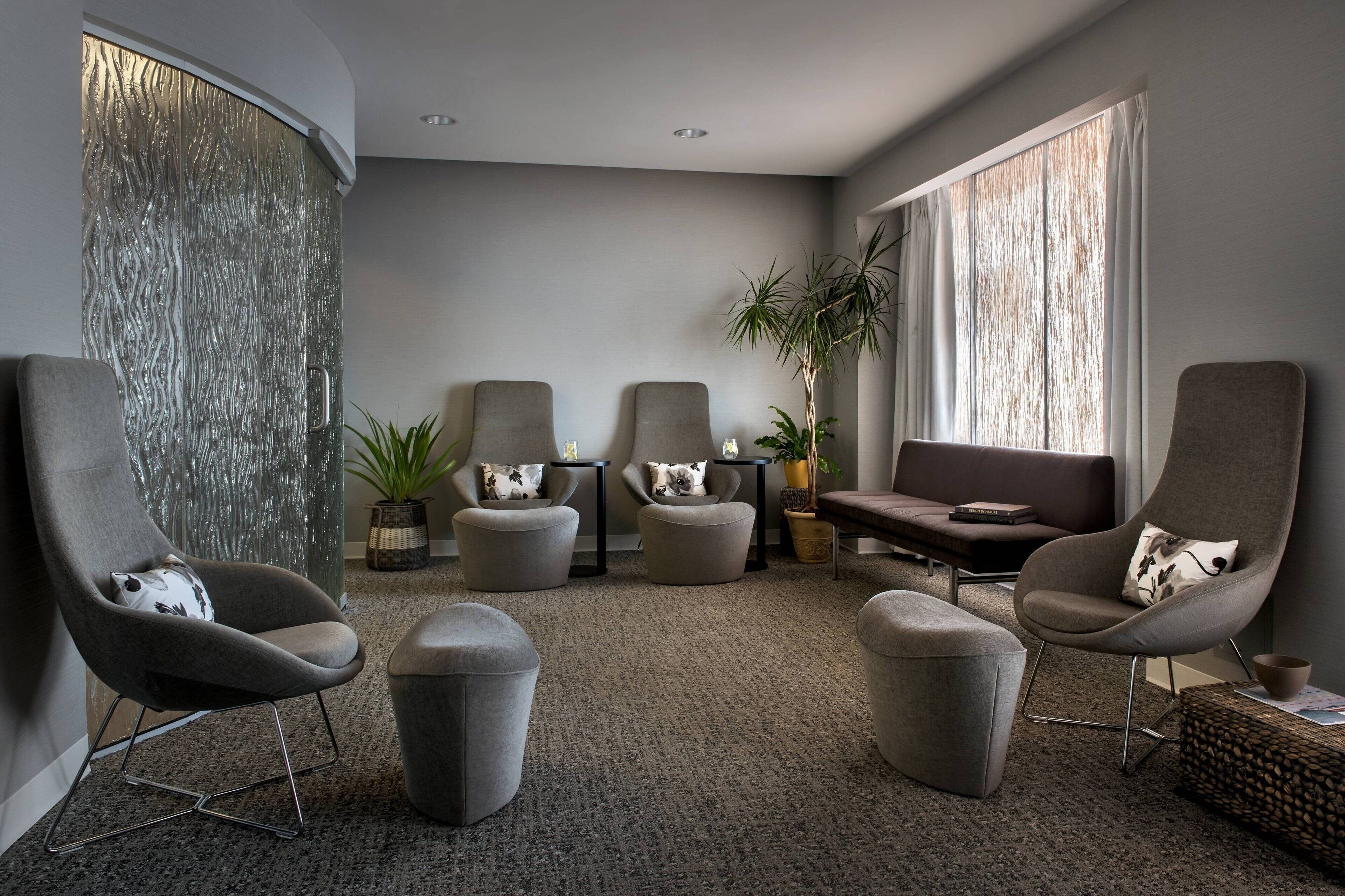 A modern living room with grey upholstered chairs, a grey sofa, and a large window with sheer curtains.