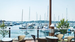 Un port de plaisance où de nombreux bateaux sont amarrés, avec une vue sur l’eau et des espaces de détente en plein air, comprenant des chaises et des tables en osier.