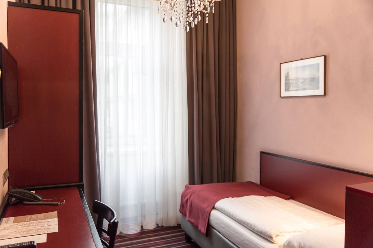 A hotel room with a bed, a desk with a chair, a telephone, and a picture on the wall.