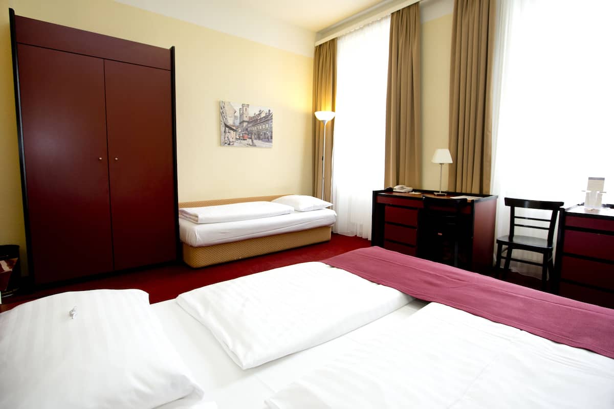 A hotel room with a bed, a desk, a chair, a wardrobe, and a painting on the wall.