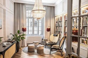 A room with a large chandelier, bookshelves, a rattan chair, and a round coffee table. - Fuerst Metternich (Vienna)