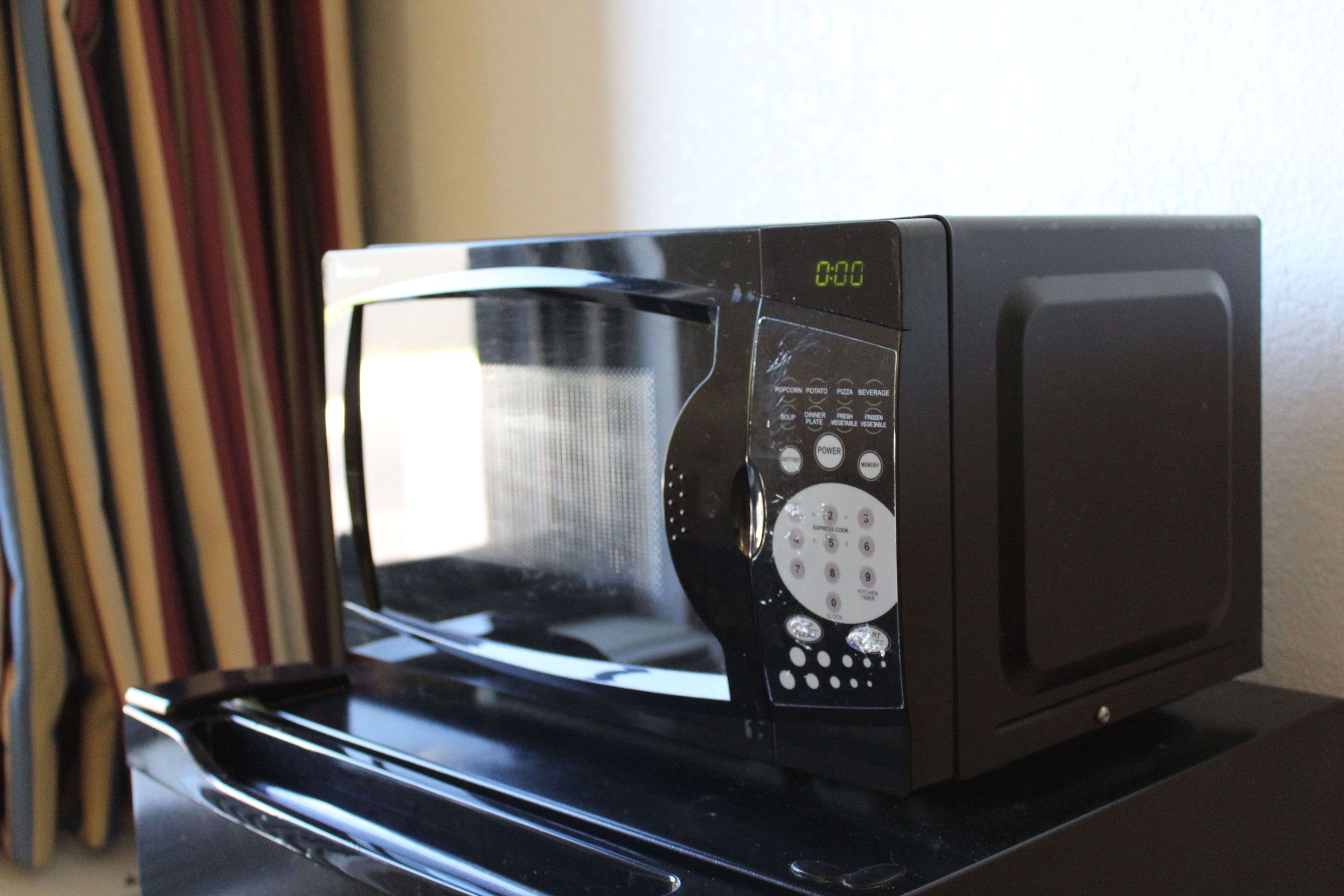 A microwave with a digital display and control panel, placed on a black surface.