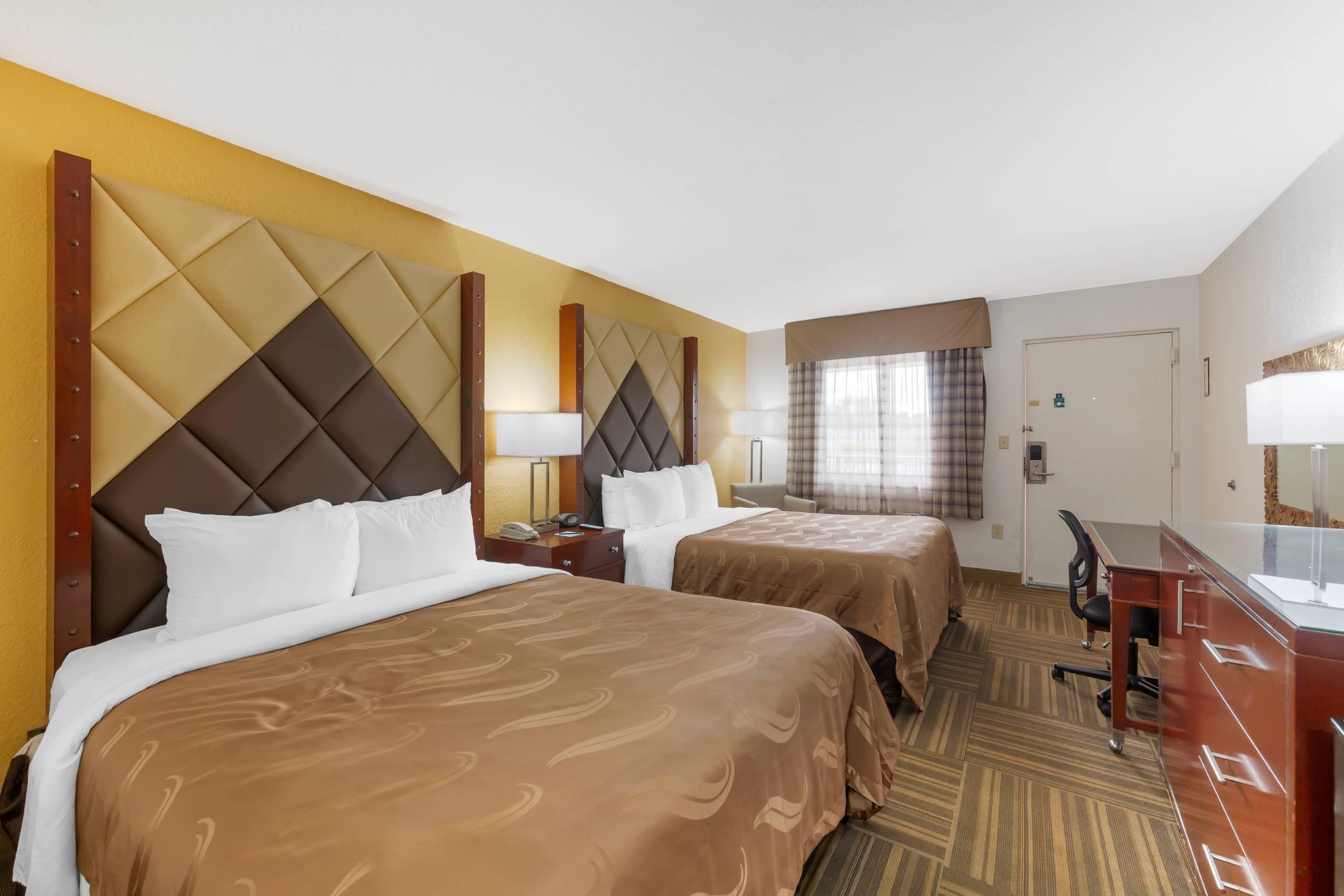A hotel room with two beds, a desk, and a chair.