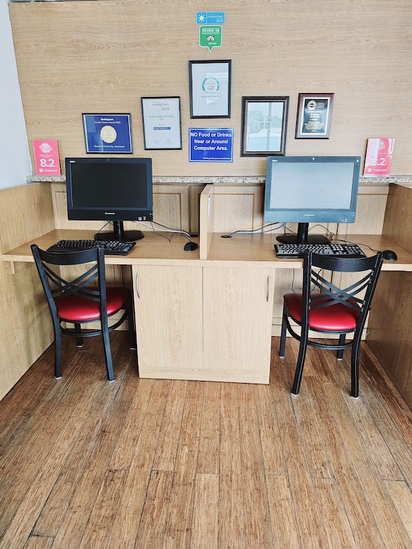 A reception desk with two computer stations, each with a monitor, keyboard, and chair. There are framed awards and certificates on the wall, and a sign indicating no food or drinks near the computer area. - Quality Inn Florida City - Gateway to the Keys (Florida City)